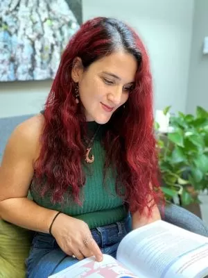 red haired woman in a green shirt with a plant in the background